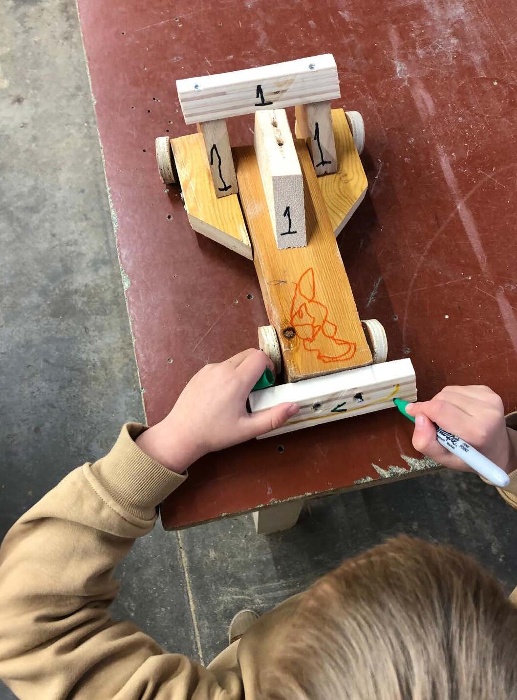 A child personalising a wooden Recup Racecar built from recovered material